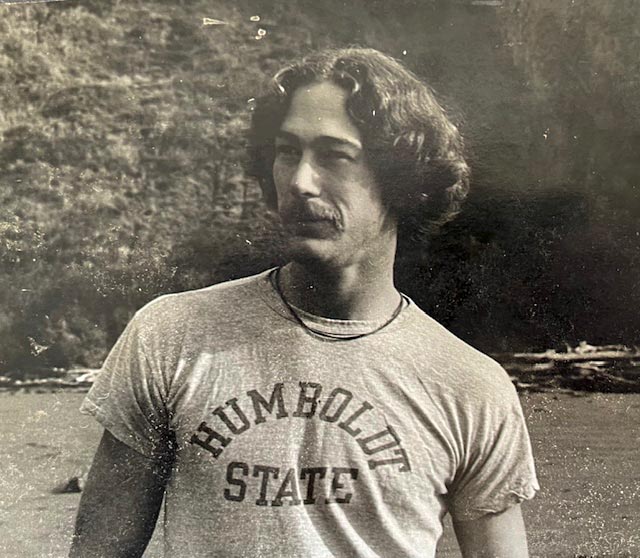 A man wearing a t-shirt that reads Humboldt State stands casually, showcasing school spirit