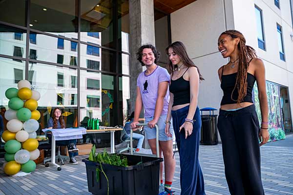 Three young students standing together in front of a modern building, smiling and engaged in conversation