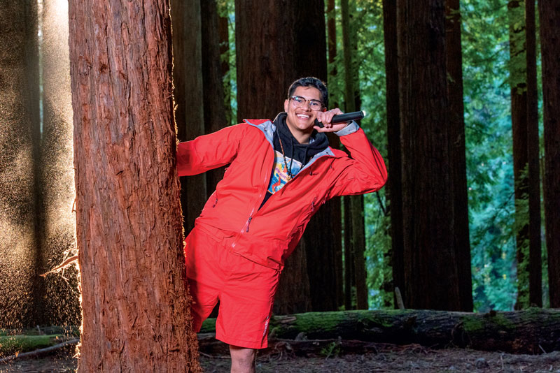 a student with a microphone peeking out from behind a tree